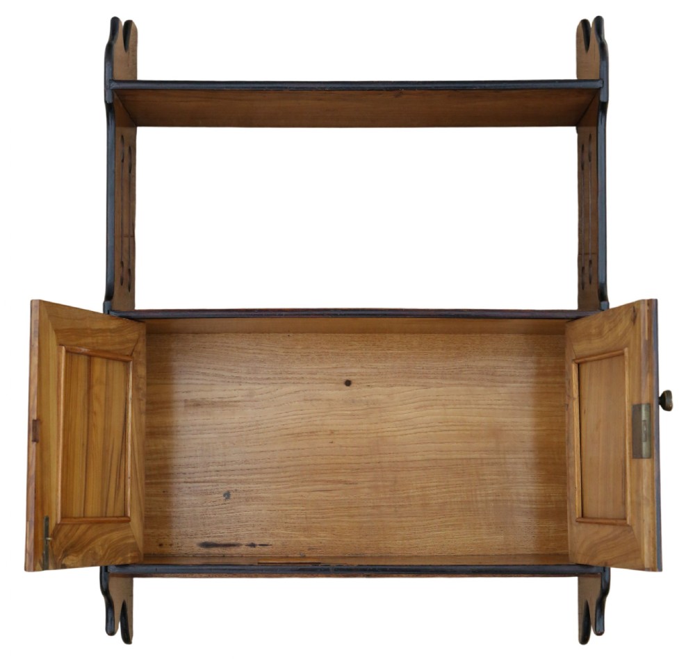 A 19th-century warm brown limewood wall cabinet featuring an upper open shelf, shaped side panels with vertical cutouts, and a lower two-door cupboard framed with dark ebonised mouldings. View IV