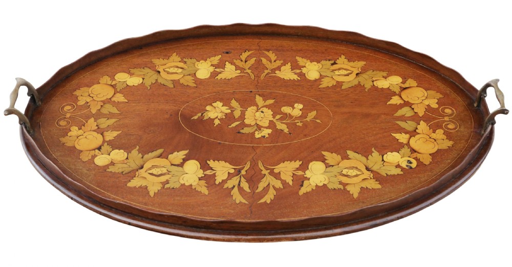 An oval mahogany serving tray featuring detailed floral marquetry inlay, a scalloped rim, and two cast brass handles.