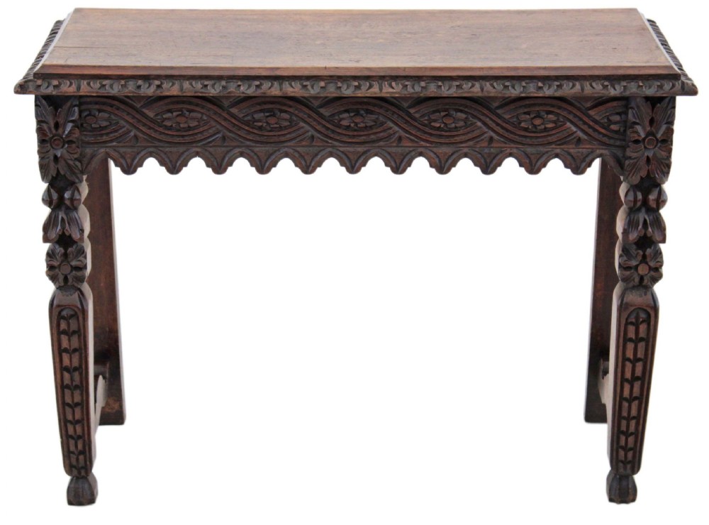 A 19th-century Victorian dark oak writing table featuring relief carving along the frieze, a scalloped apron, and carved end legs.