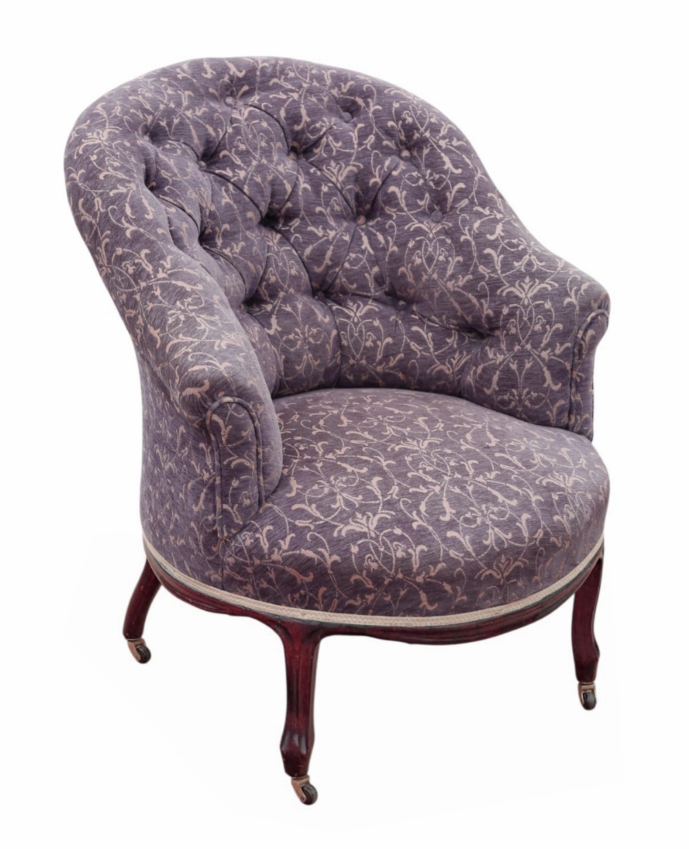 An antique Victorian tub armchair upholstered in patterned dusty purple fabric with a button-tufted backrest and mahogany legs on brass castors.