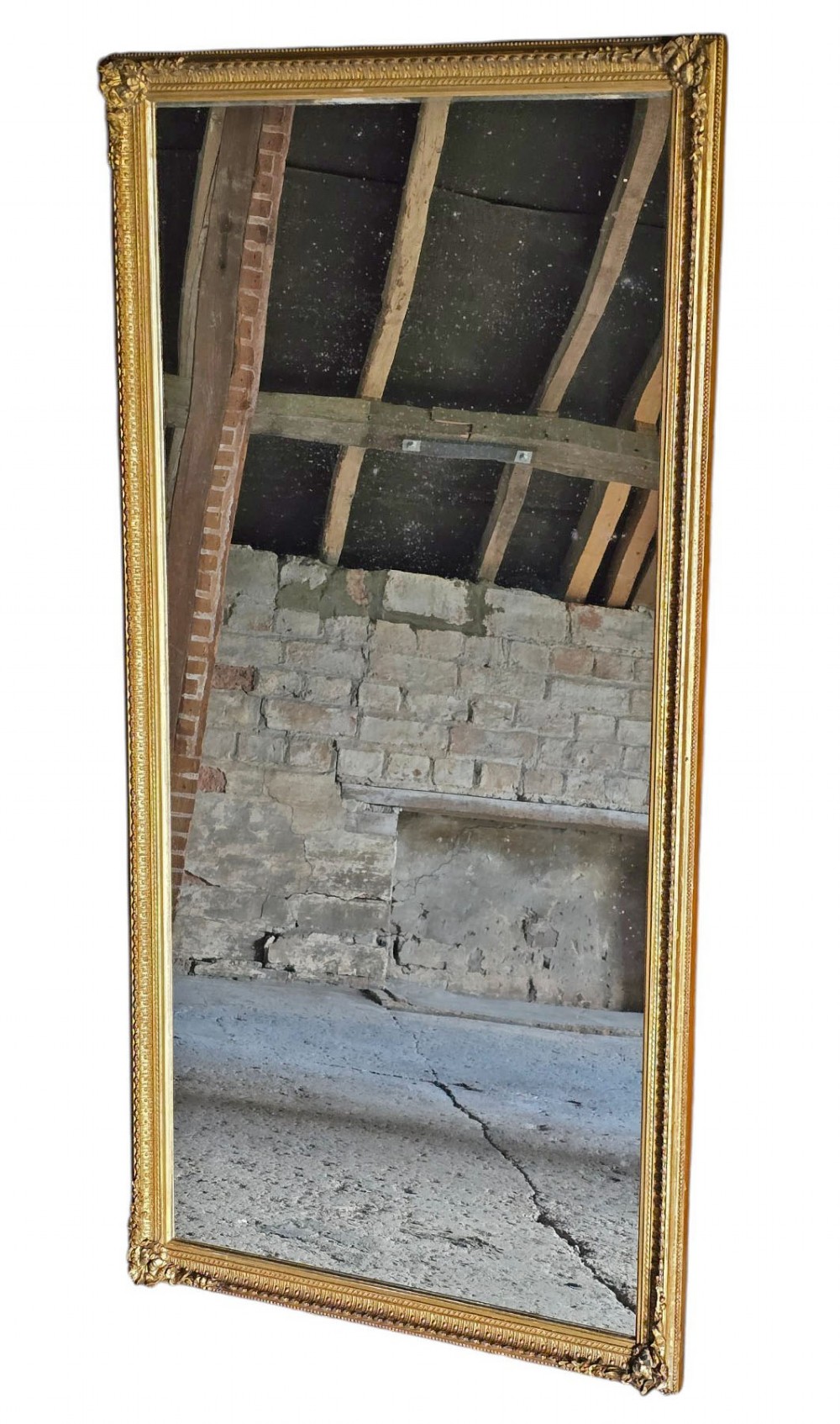 A tall rectangular full-length mirror with a gilded frame featuring delicate beaded moulding and acanthus leaf corner ornaments.