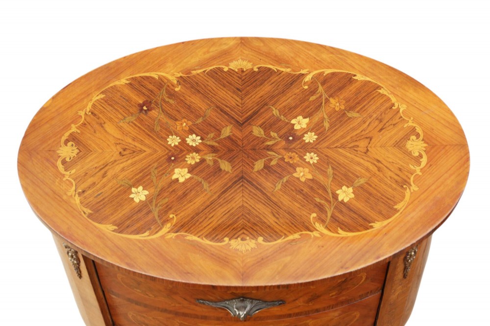 A pair of French oval bedside tables with floral marquetry inlay, three drawers, gilt mounts, and slender cabriole legs. View V