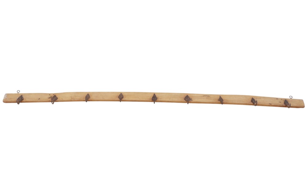 A long horizontal pine timber rail fitted with nine spaced, hand-forged wrought iron hooks with pointed backplates. View V
