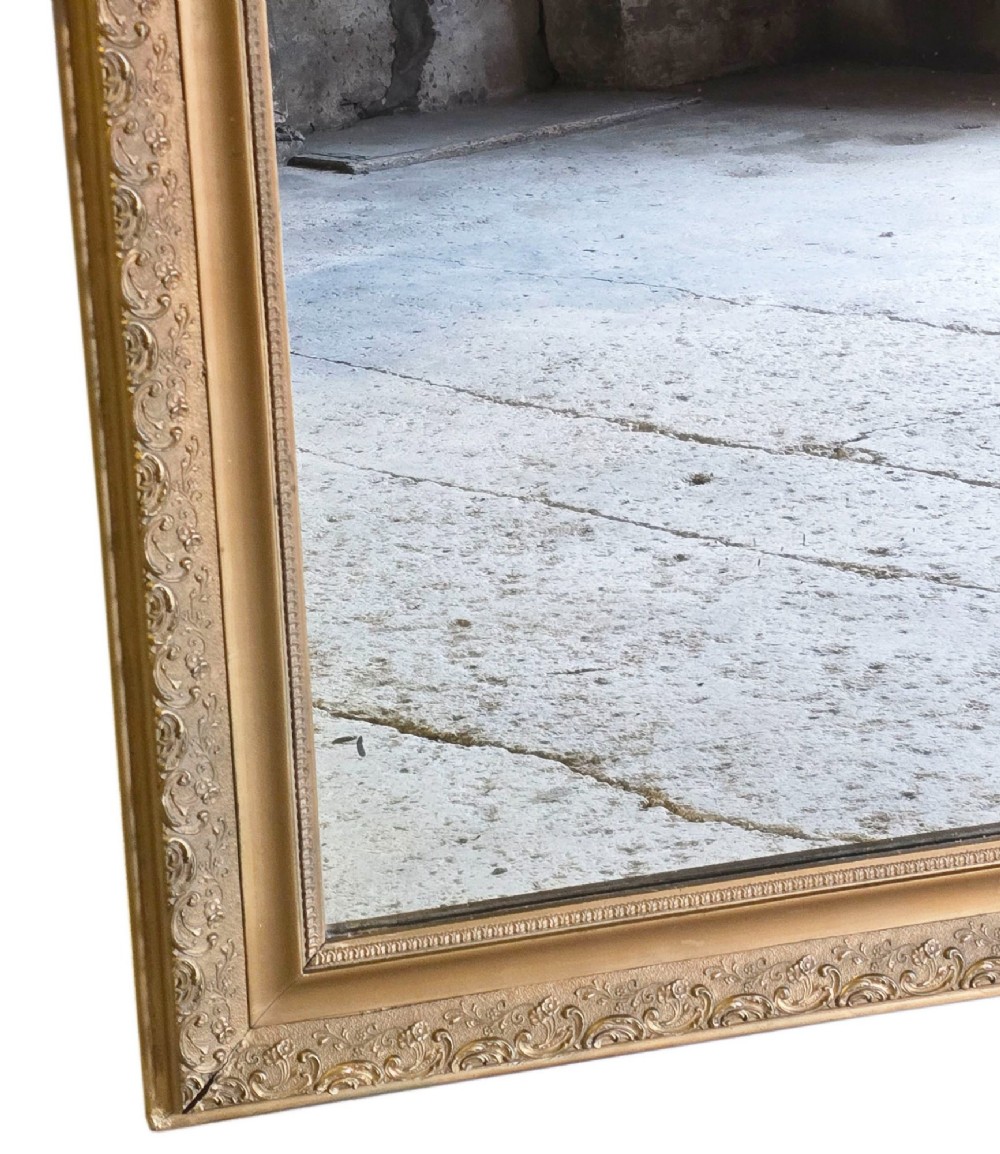 A large late nineteenth-century rectangular overmantel mirror with rounded upper corners, an intricate foliate carved gilt frame, and a beaded inner border. View V