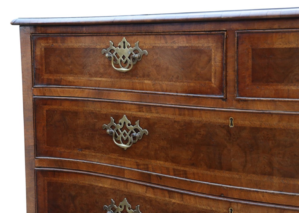 A serpentine-front burr walnut chest of drawers featuring crossbanded borders, cast brass handles, and ogee bracket feet. View V