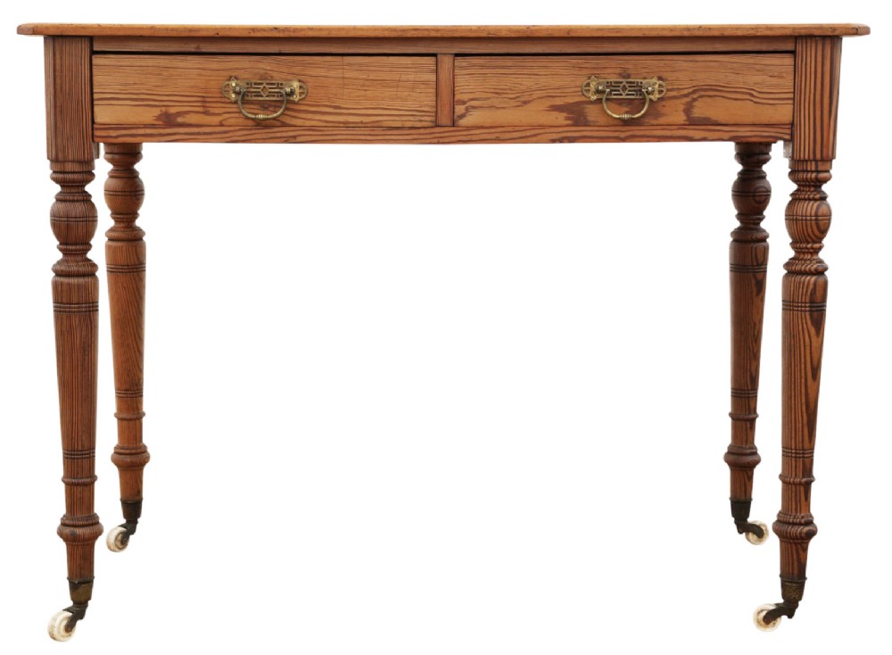 A 19th-century pitch pine writing table with two drawers, brass handles, turned legs, and metal castors.