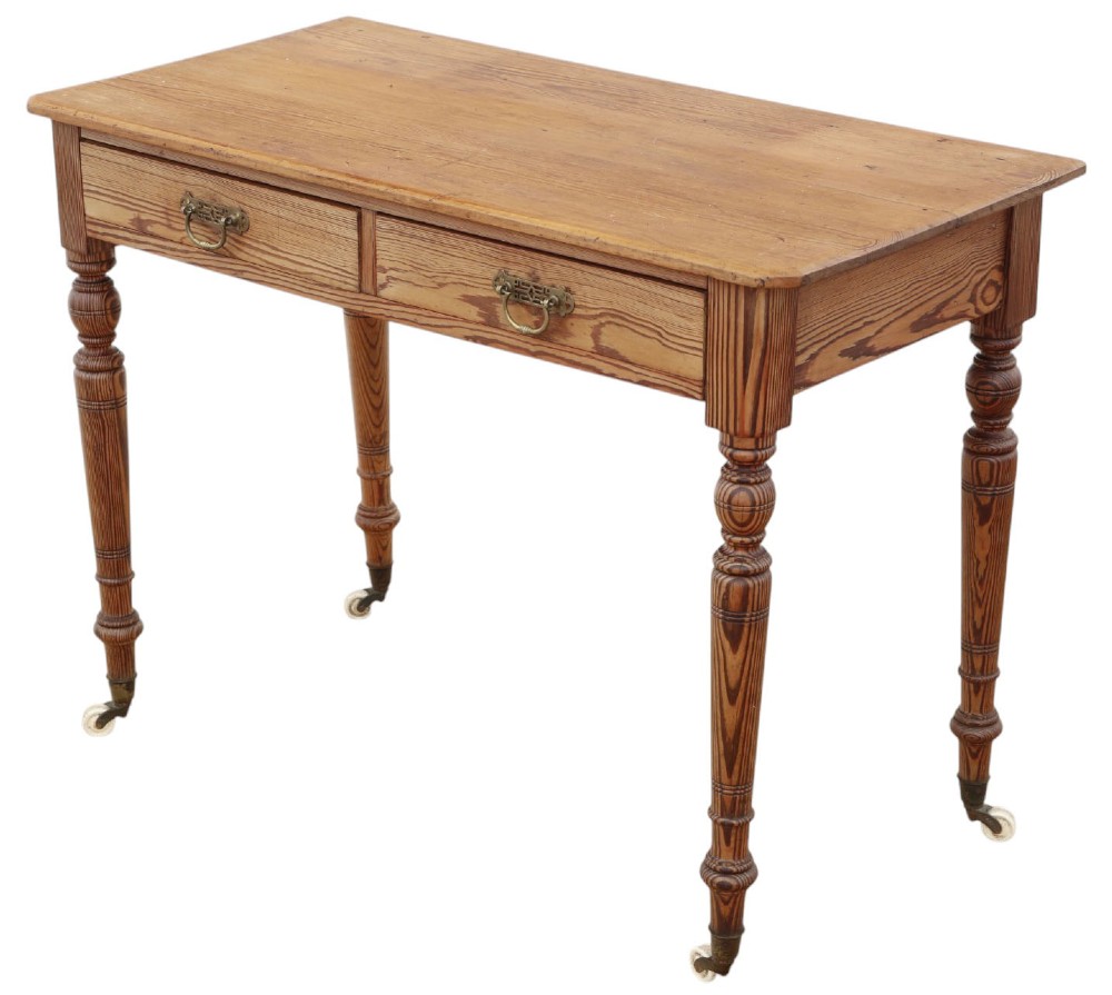 A 19th-century pitch pine writing table with two drawers, brass handles, turned legs, and metal castors. View V