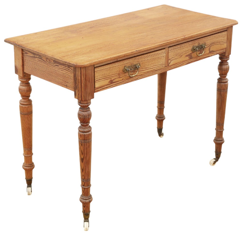 A 19th-century pitch pine writing table with two drawers, brass handles, turned legs, and metal castors. View VI
