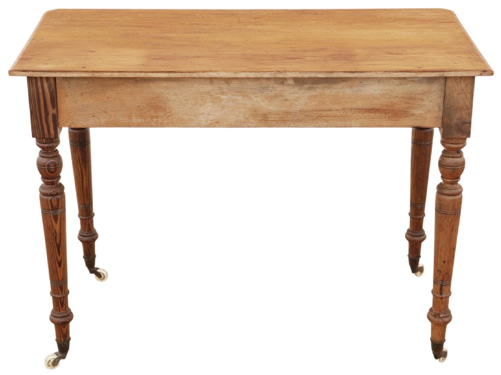 A 19th-century pitch pine writing table with two drawers, brass handles, turned legs, and metal castors. View VII