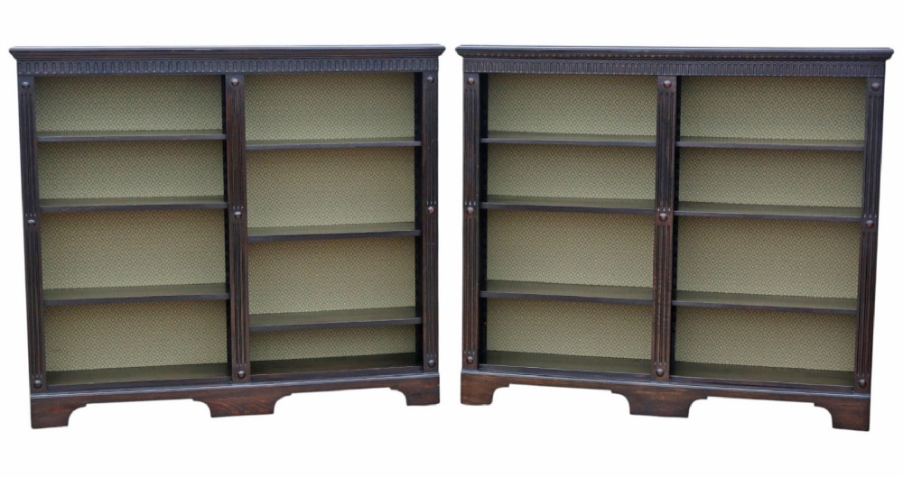 A matching pair of dark oak double-bay bookcases featuring fluted vertical trim, adjustable shelving, green pattern-lined interiors, and bracket bases.