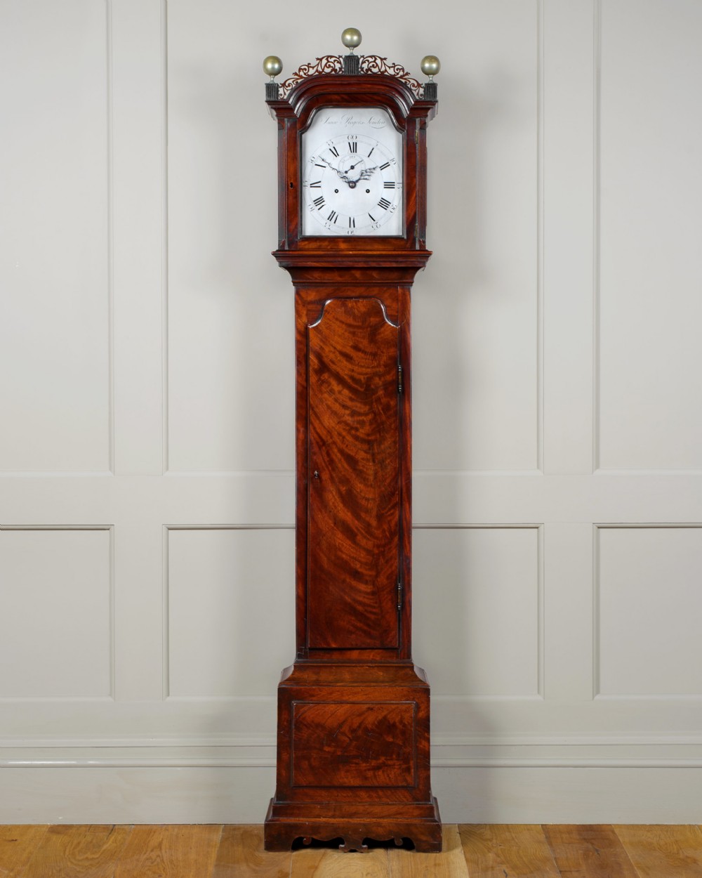 An 18th-century Georgian flame mahogany longcase clock featuring an arched dial, brass finials, and a tall wooden case on bracket feet.