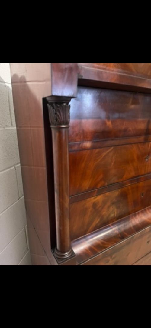 A 19th-century Biedermeier flame mahogany secretaire chest featuring a fall-front desk section, side column supports, and multiple storage drawers. View VI