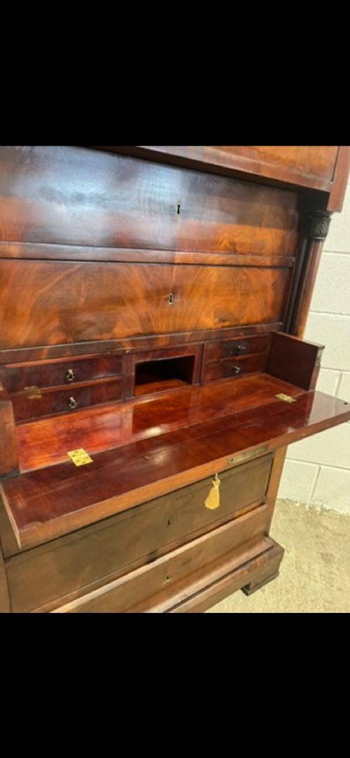 A 19th-century Biedermeier flame mahogany secretaire chest featuring a fall-front desk section, side column supports, and multiple storage drawers. View IX
