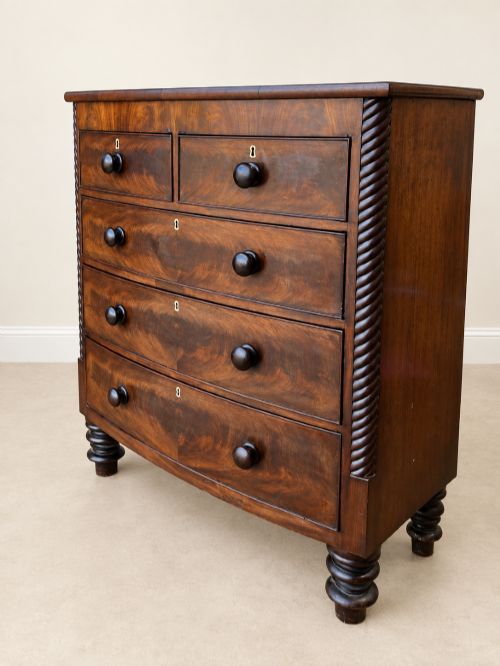 fig 1. A 19th-century mahogany bowfront chest of drawers featuring spiral rope-twist pilasters, turned wooden knobs, and brass keyhole escutcheons.
