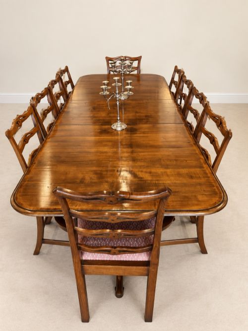 fig 1. A large extendable mahogany dining table surrounded by ten matching wooden chairs with patterned pink fabric seats.