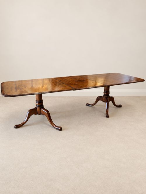 fig 2. A large extendable mahogany dining table surrounded by ten matching wooden chairs with patterned pink fabric seats.