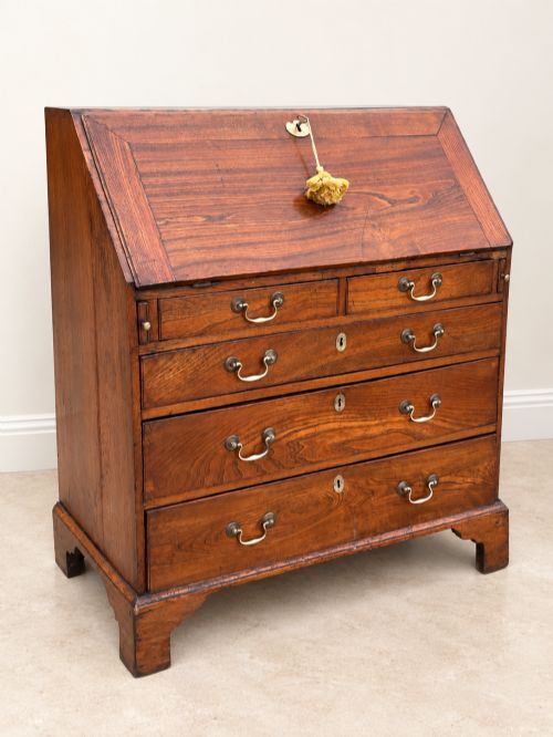 fig 1. An antique Georgian warm brown elm slant-front writing bureau with four drawers, brass handles, and bracket feet.