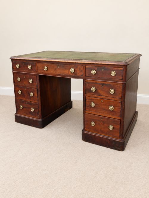 fig 1. A 19th-century dark mahogany pedestal desk featuring nine drawers with brass handles and an inset green leather writing surface.