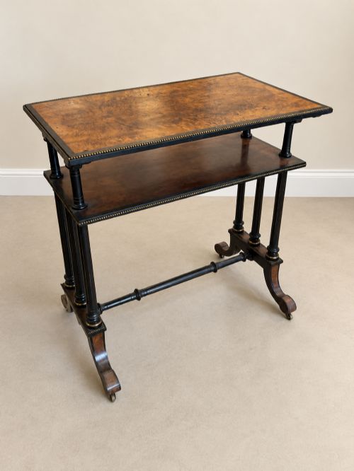 fig 1. A 19th-century two-tier side table with a burr walnut surface, ebonised turned column legs, brass beaded borders, and scrolled feet on castors.