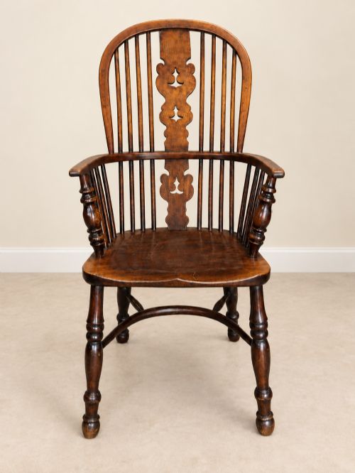fig 1. An antique 19th-century wooden Windsor armchair featuring a hoop back with turned spindles, a central pierced splat, a contoured saddle seat, and curved armrests supported by turned front legs.
