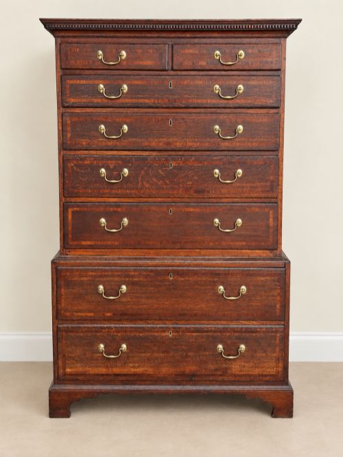 fig 1. An antique Georgian oak chest on chest featuring two small top drawers over five full-width graduated drawers with brass swan-neck handles and bracket feet.
