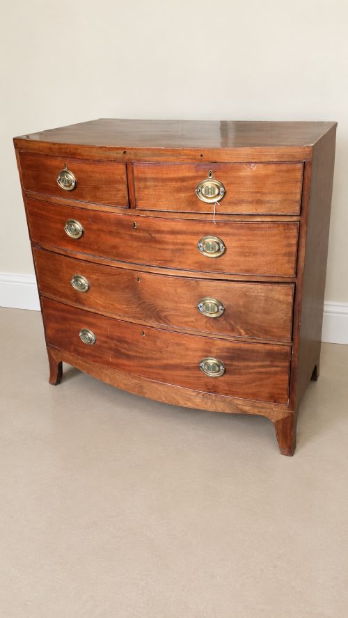 A nineteenth-century mahogany bowfront chest of drawers featuring two short drawers above three long graduated drawers with oval brass handles and splayed bracket feet. View II