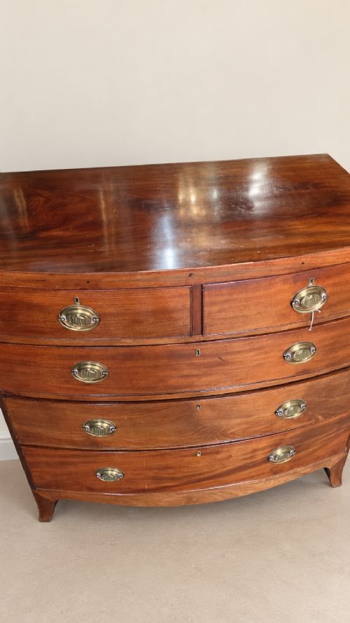 A nineteenth-century mahogany bowfront chest of drawers featuring two short drawers above three long graduated drawers with oval brass handles and splayed bracket feet. View IV