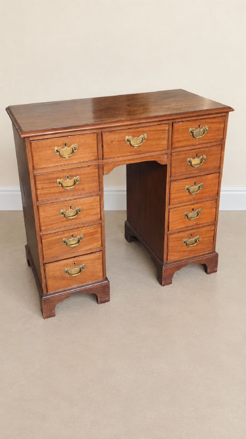 A 19th-century mahogany kneehole desk featuring multiple side drawers with brass batwing handles, a central recessed kneehole, and bracket feet. View II