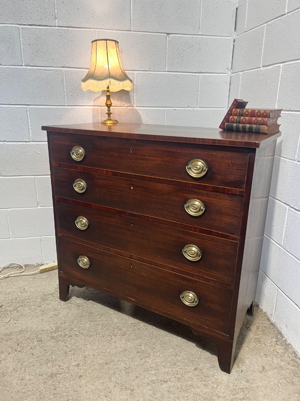 A nineteenth-century mahogany chest of drawers featuring four graduated drawers with oval brass handles and bracket feet. View II
