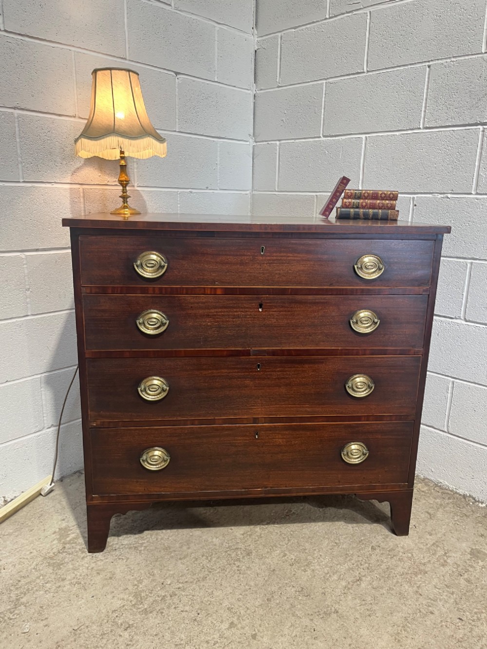 A nineteenth-century mahogany chest of drawers featuring four graduated drawers with oval brass handles and bracket feet. View V