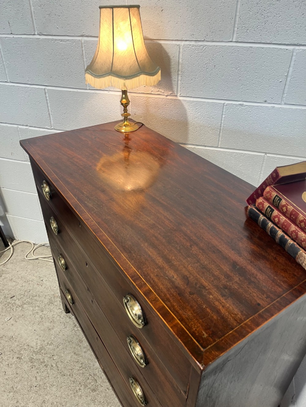 A nineteenth-century mahogany chest of drawers featuring four graduated drawers with oval brass handles and bracket feet. View VI