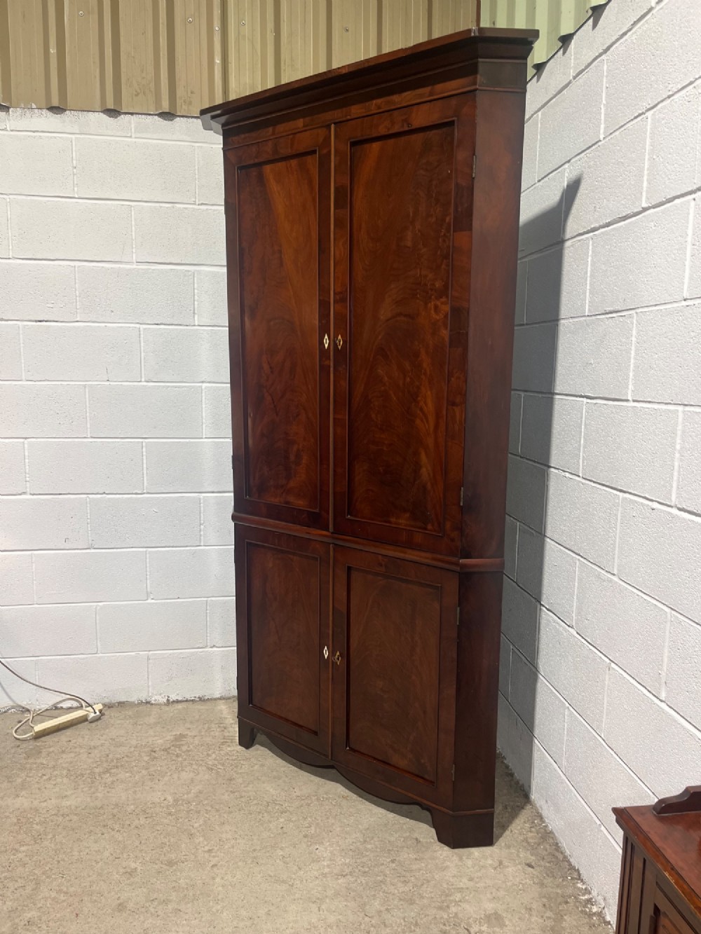 A tall Georgian floor-standing corner cupboard made of dark flame mahogany, featuring two upper doors and two lower doors with brass diamond escutcheons. View II