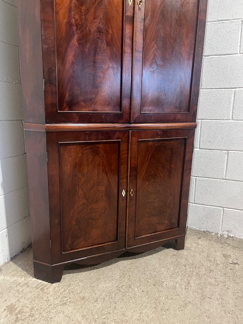A tall Georgian floor-standing corner cupboard made of dark flame mahogany, featuring two upper doors and two lower doors with brass diamond escutcheons. View V