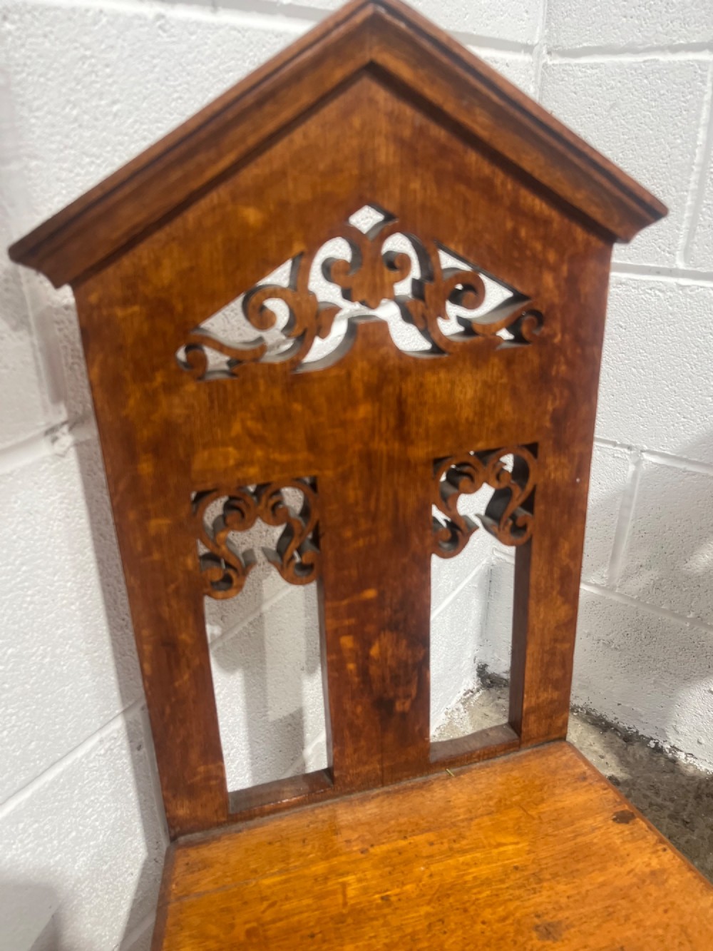 A pair of 19th-century carved oak hall chairs with pointed pediment tops, pierced fretwork back splats, flat timber seats, and turned front legs. View VI