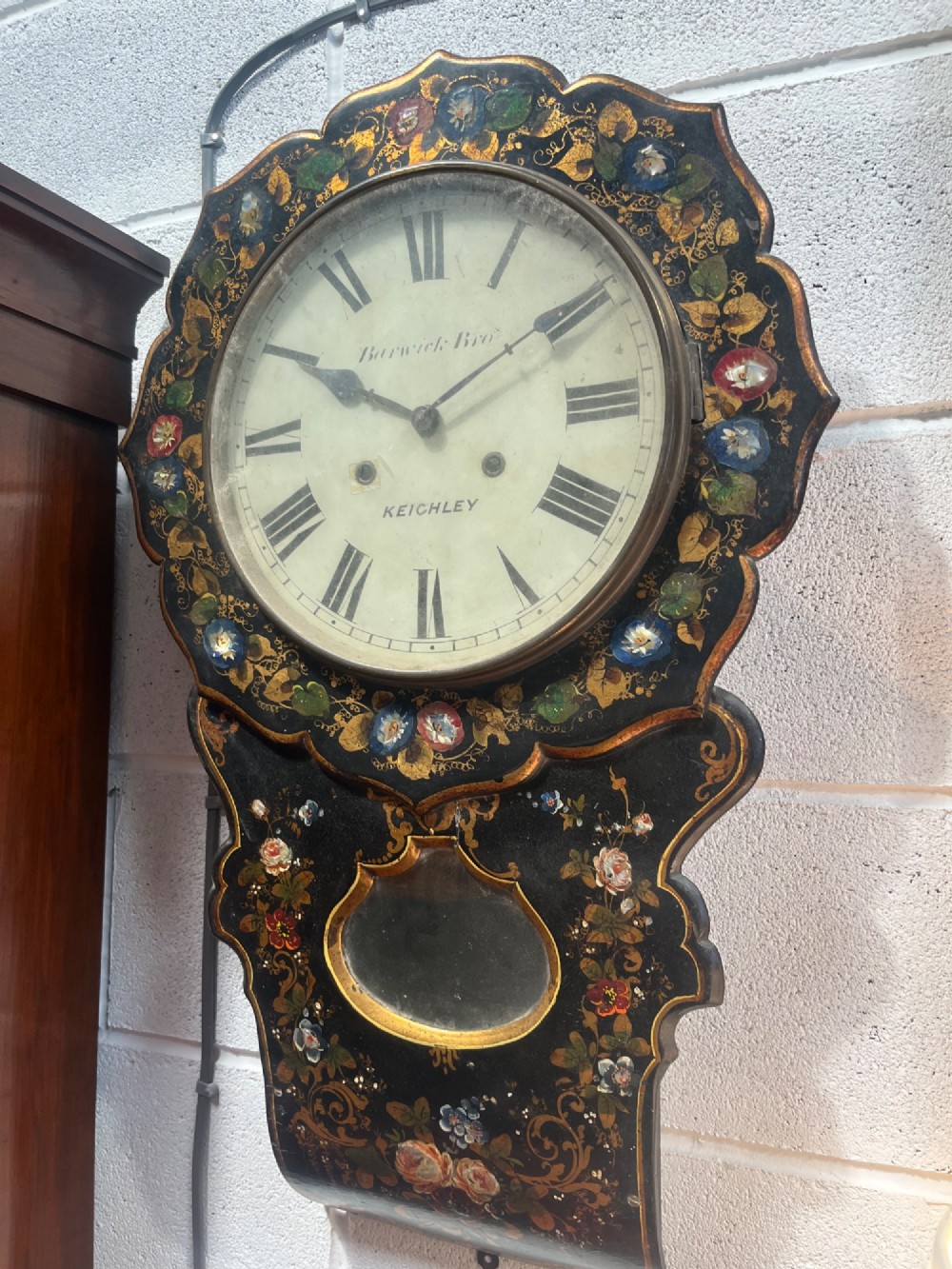 A 19th-century Victorian wall clock featuring a scalloped ebonised case decorated with gilt scrollwork and polychrome floral painting around a cream dial with Roman numerals. View II