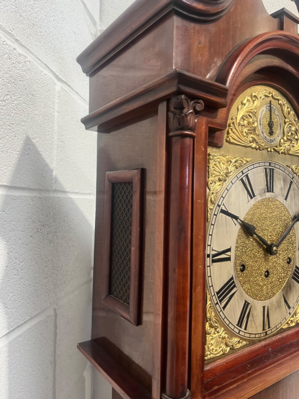 An antique Edwardian mahogany longcase clock featuring a swan-neck pediment, brass arch dial with Roman numerals, and an arched trunk door. View VII
