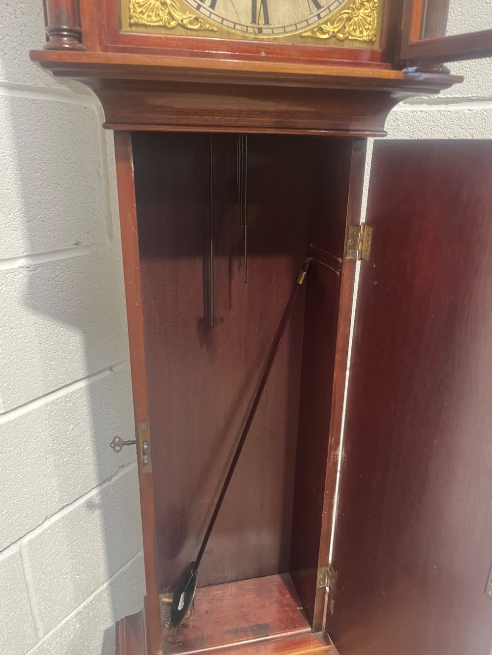 An antique Edwardian mahogany longcase clock featuring a swan-neck pediment, brass arch dial with Roman numerals, and an arched trunk door. View XI