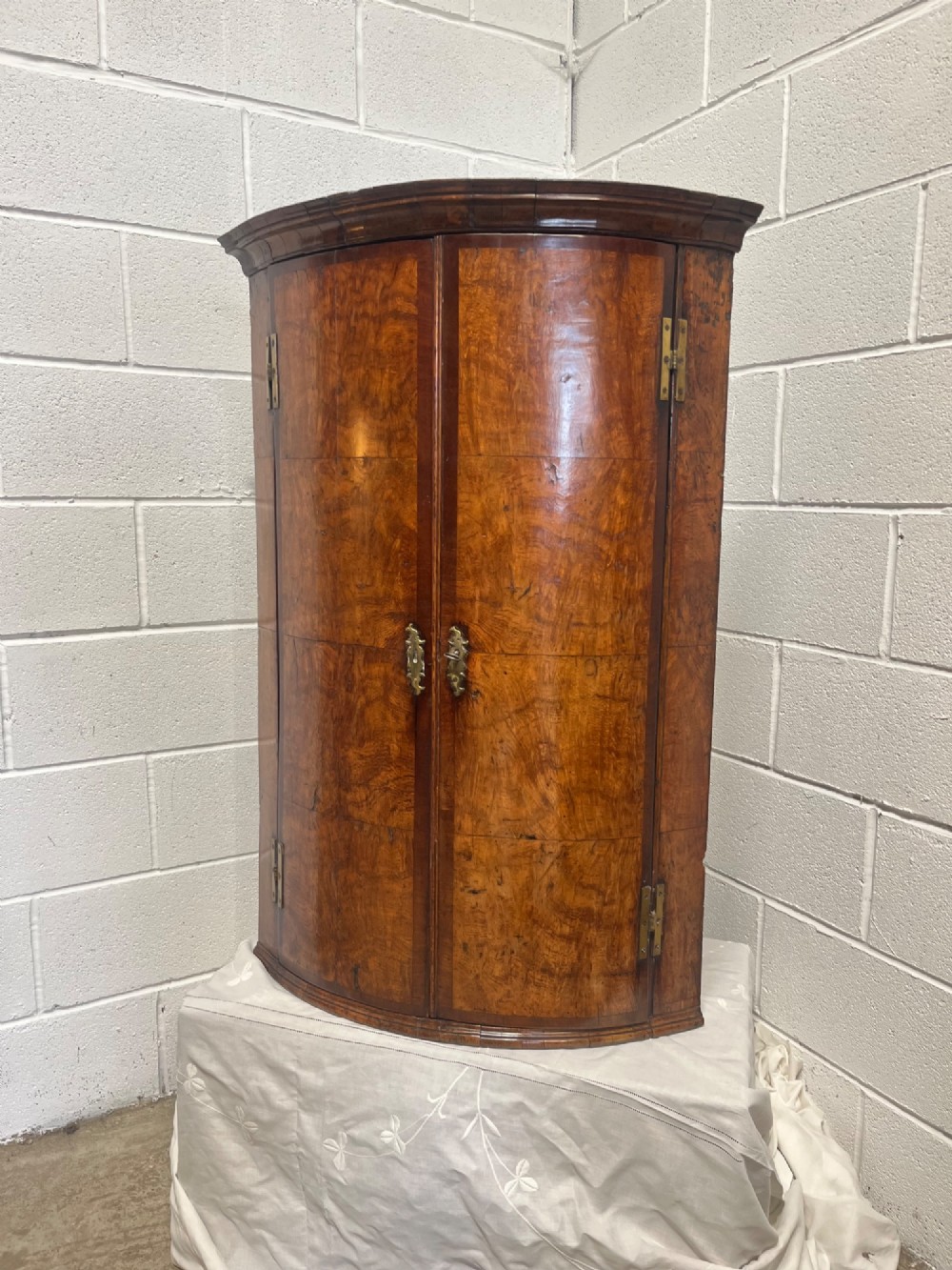 A George III bowfront corner cupboard crafted from figured burr oak timber featuring double doors with brass H-hinges. View II