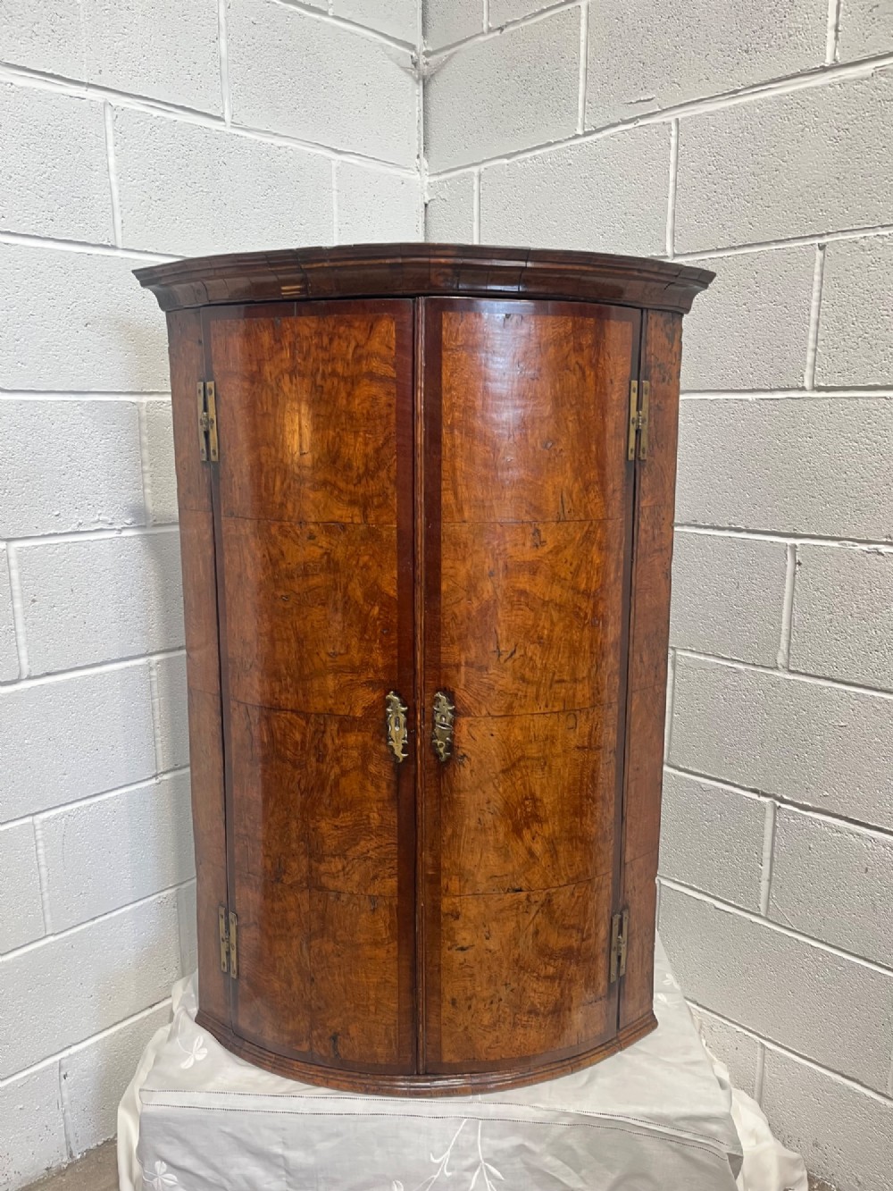 A George III bowfront corner cupboard crafted from figured burr oak timber featuring double doors with brass H-hinges. View V