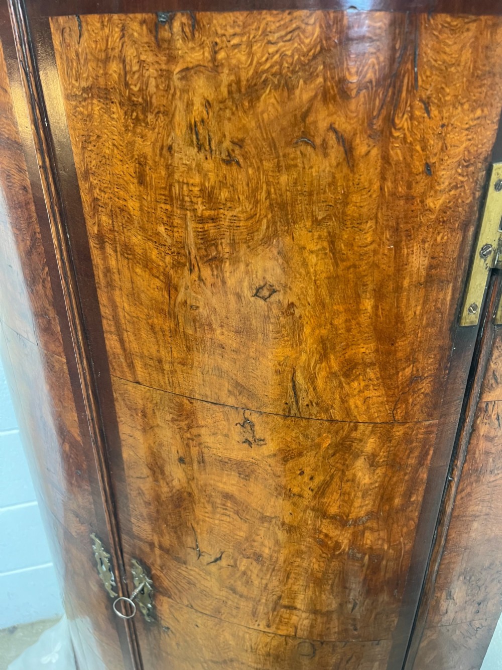 A George III bowfront corner cupboard crafted from figured burr oak timber featuring double doors with brass H-hinges. View IX