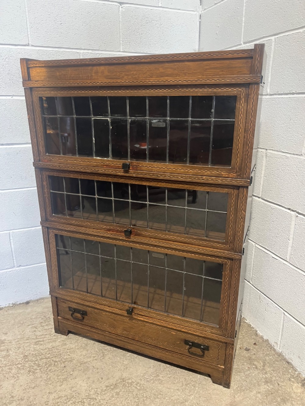 A three-tier oak sectional Globe Wernicke bookcase featuring leaded glass up-and-over doors, inlaid decorative banding, and a single bottom drawer. View II