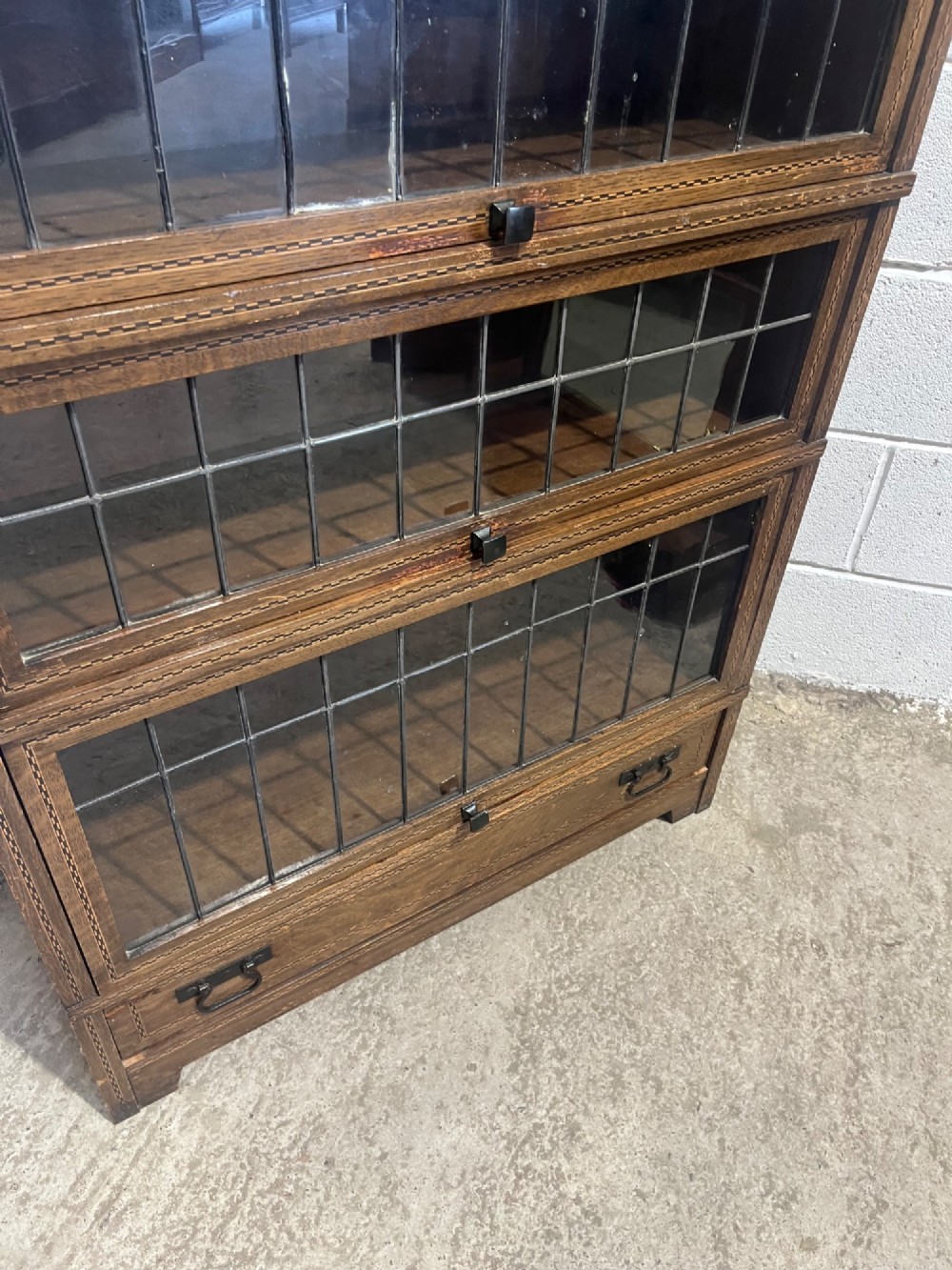 A three-tier oak sectional Globe Wernicke bookcase featuring leaded glass up-and-over doors, inlaid decorative banding, and a single bottom drawer. View VI