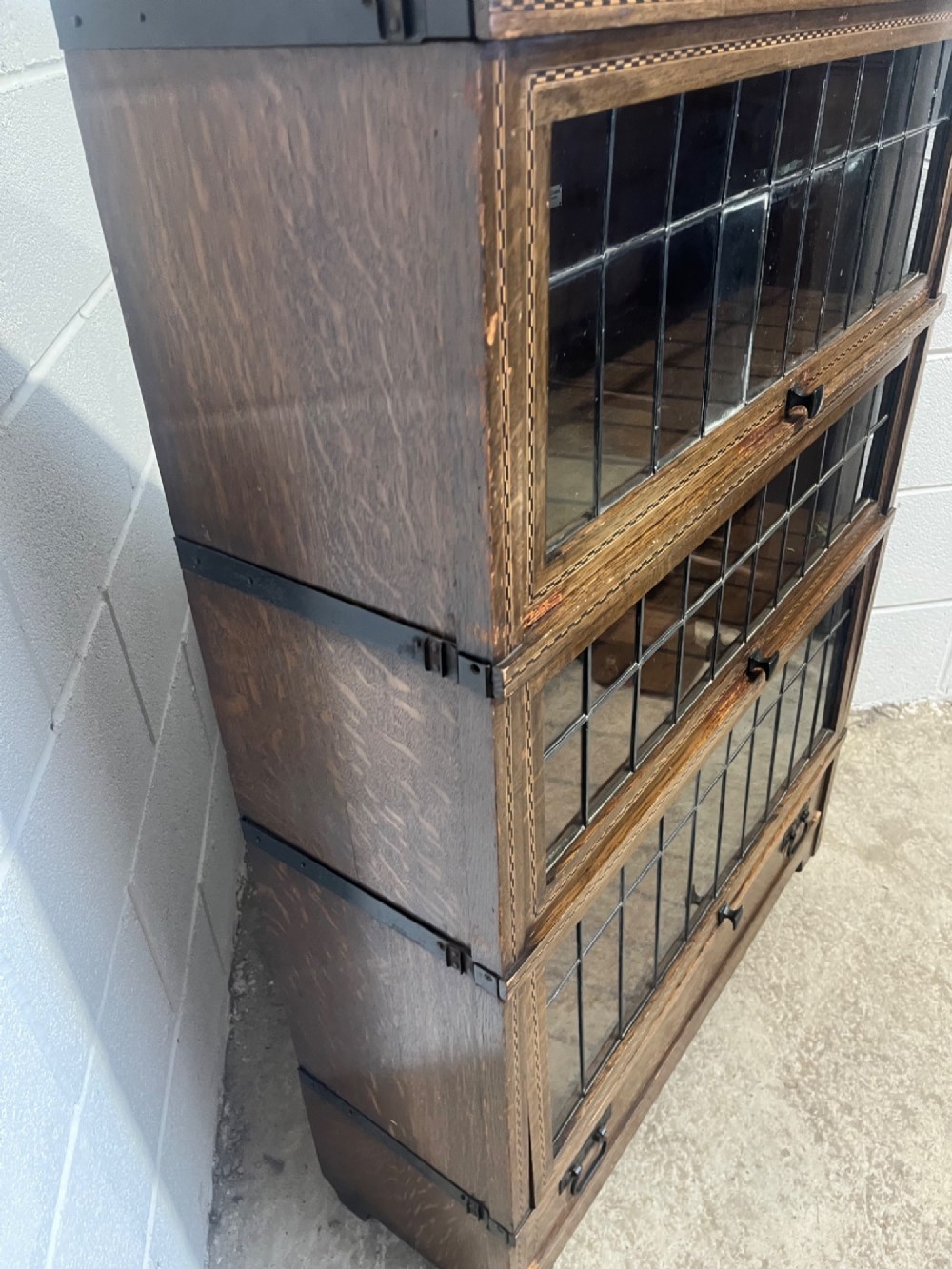 A three-tier oak sectional Globe Wernicke bookcase featuring leaded glass up-and-over doors, inlaid decorative banding, and a single bottom drawer. View VII