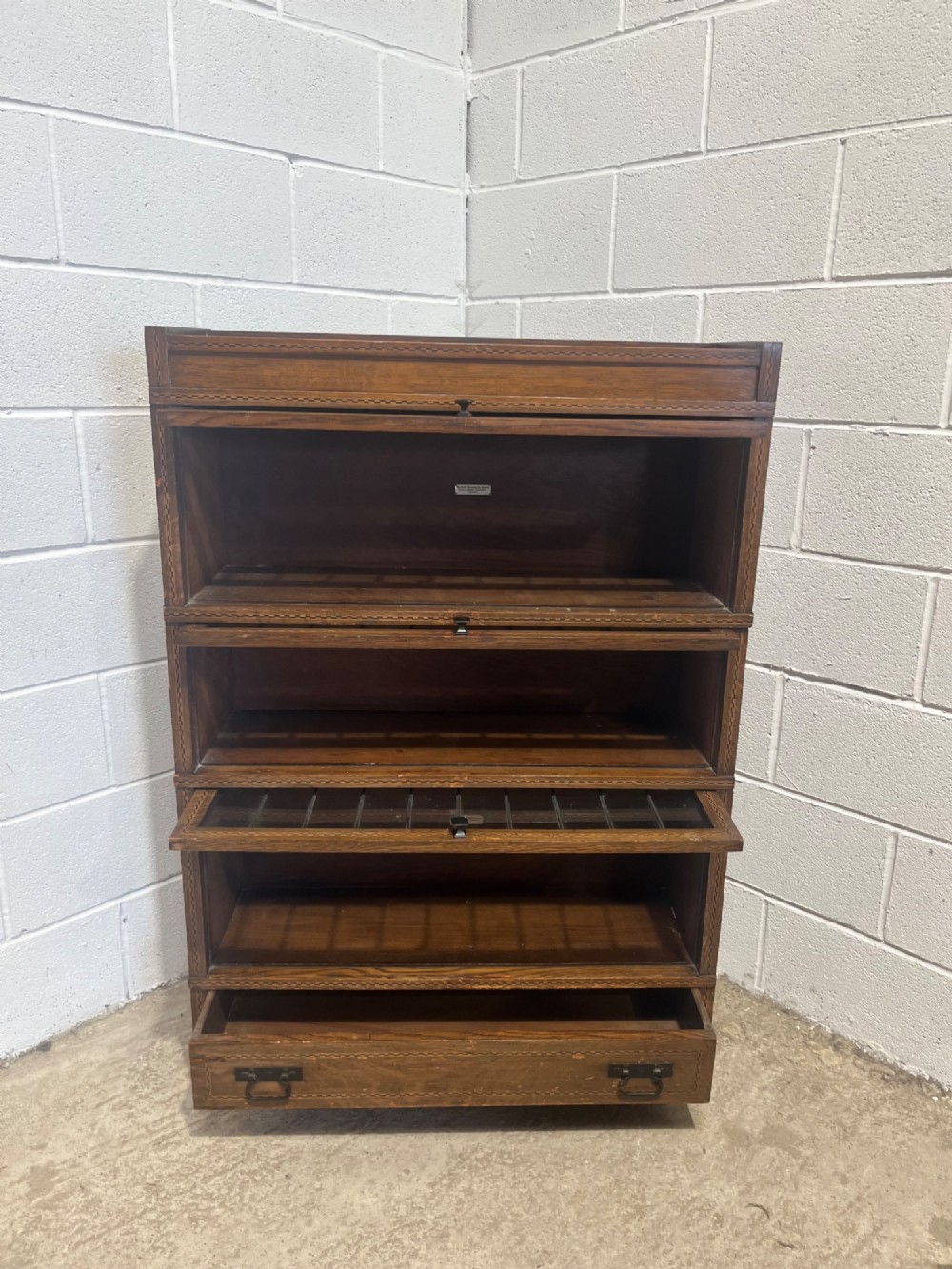 A three-tier oak sectional Globe Wernicke bookcase featuring leaded glass up-and-over doors, inlaid decorative banding, and a single bottom drawer. View X