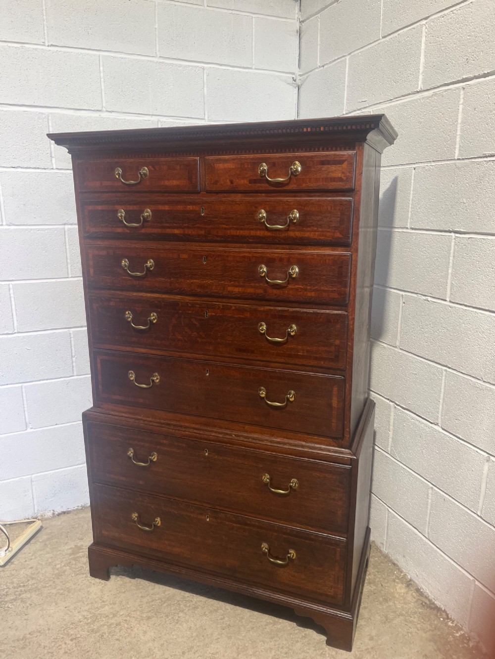 A tall George III oak chest on chest featuring brass swan-neck handles, crossbanded drawer borders, and bracket feet. View II