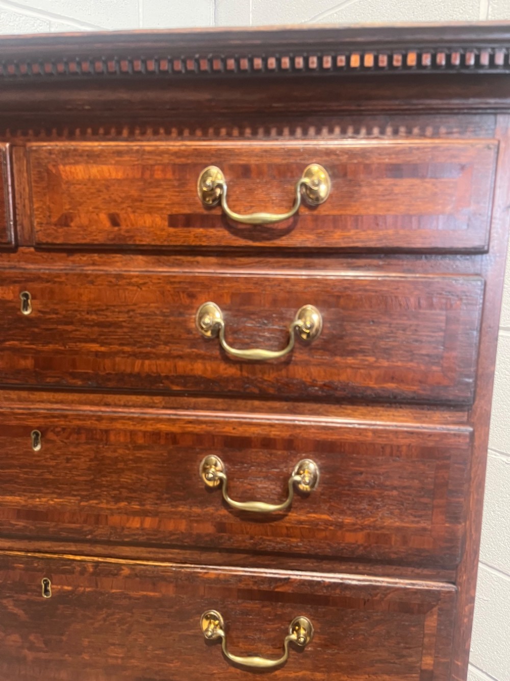 A tall George III oak chest on chest featuring brass swan-neck handles, crossbanded drawer borders, and bracket feet. View VI