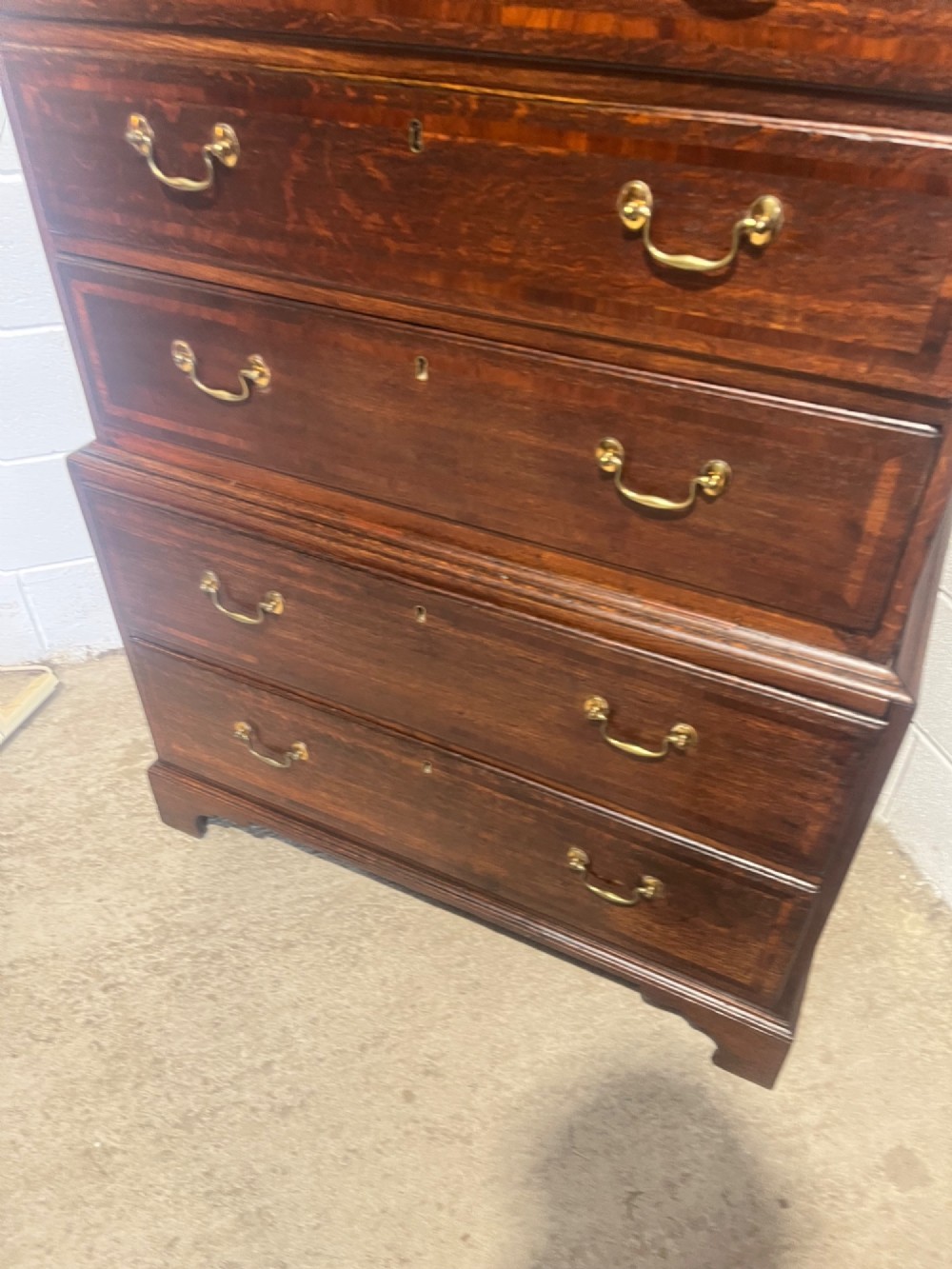 A tall George III oak chest on chest featuring brass swan-neck handles, crossbanded drawer borders, and bracket feet. View VII
