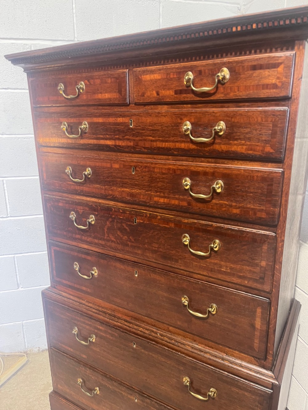 A tall George III oak chest on chest featuring brass swan-neck handles, crossbanded drawer borders, and bracket feet. View VIII