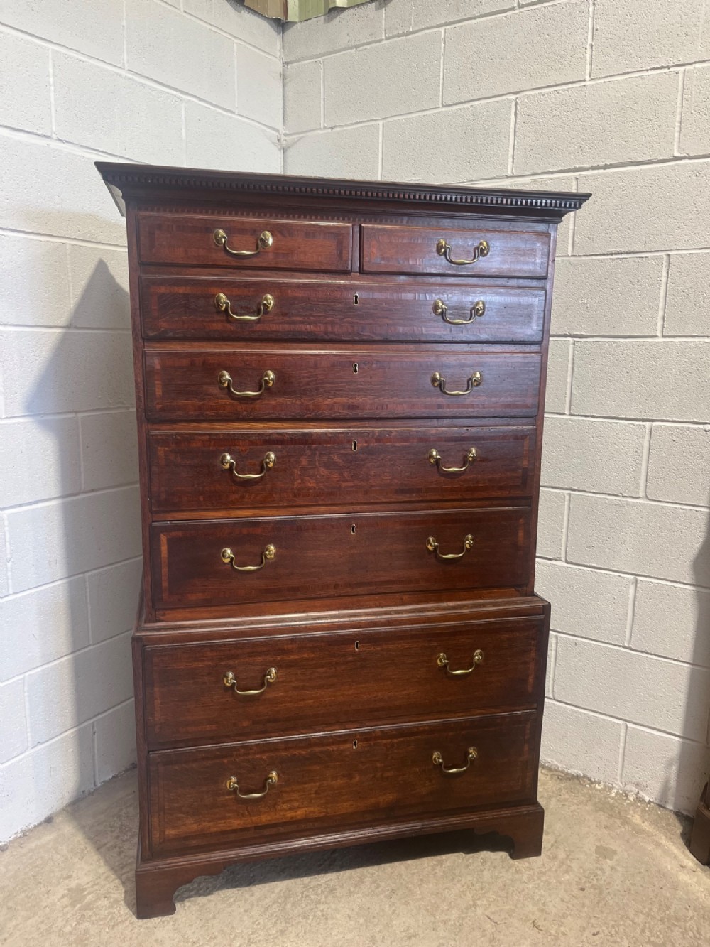A tall George III oak chest on chest featuring brass swan-neck handles, crossbanded drawer borders, and bracket feet. View XII