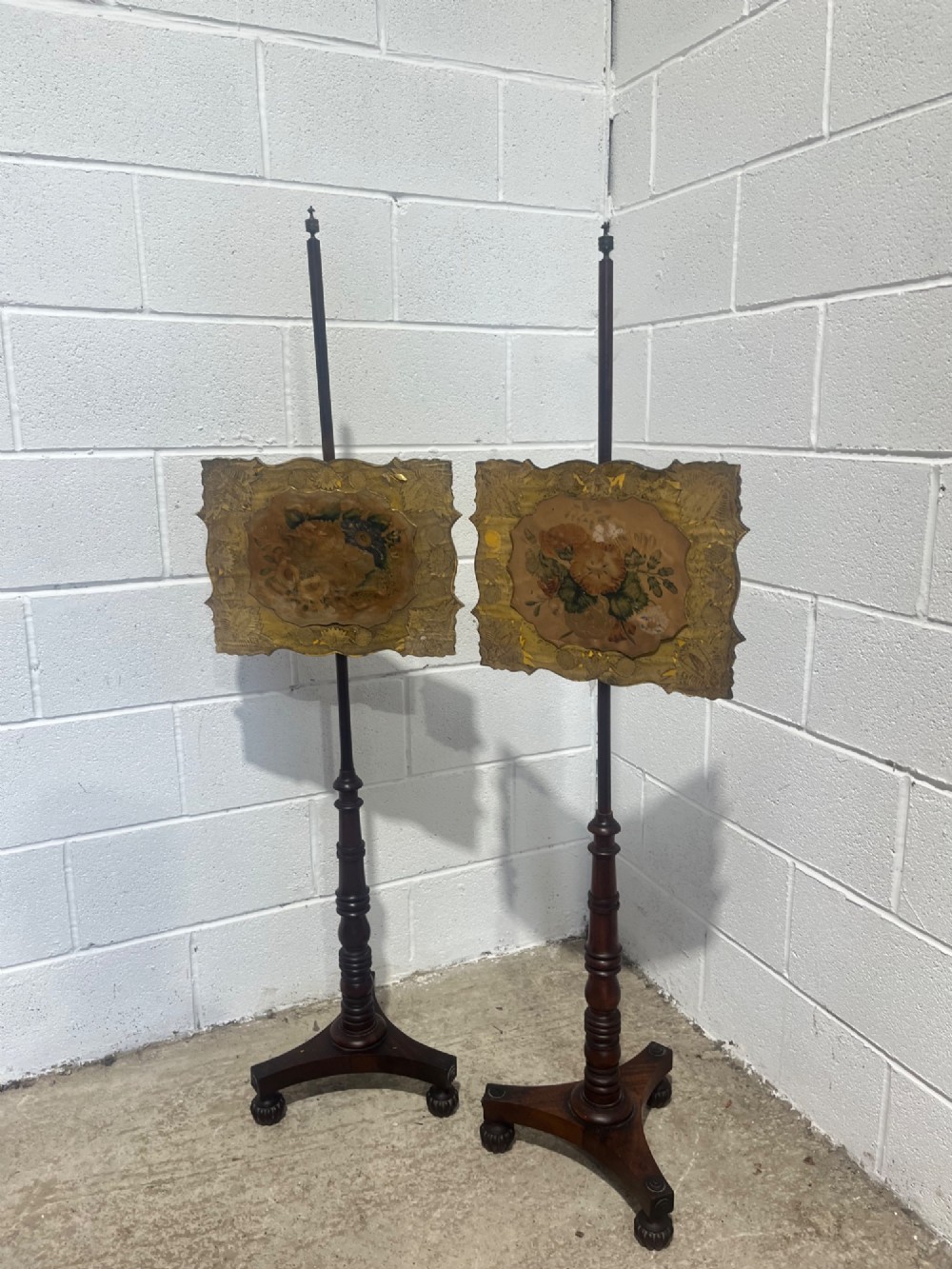 A pair of antique Regency mahogany pole screens with turned central spindles, tripod bases, and rectangular adjustable panels featuring floral paintings surrounded by gilded borders. View V